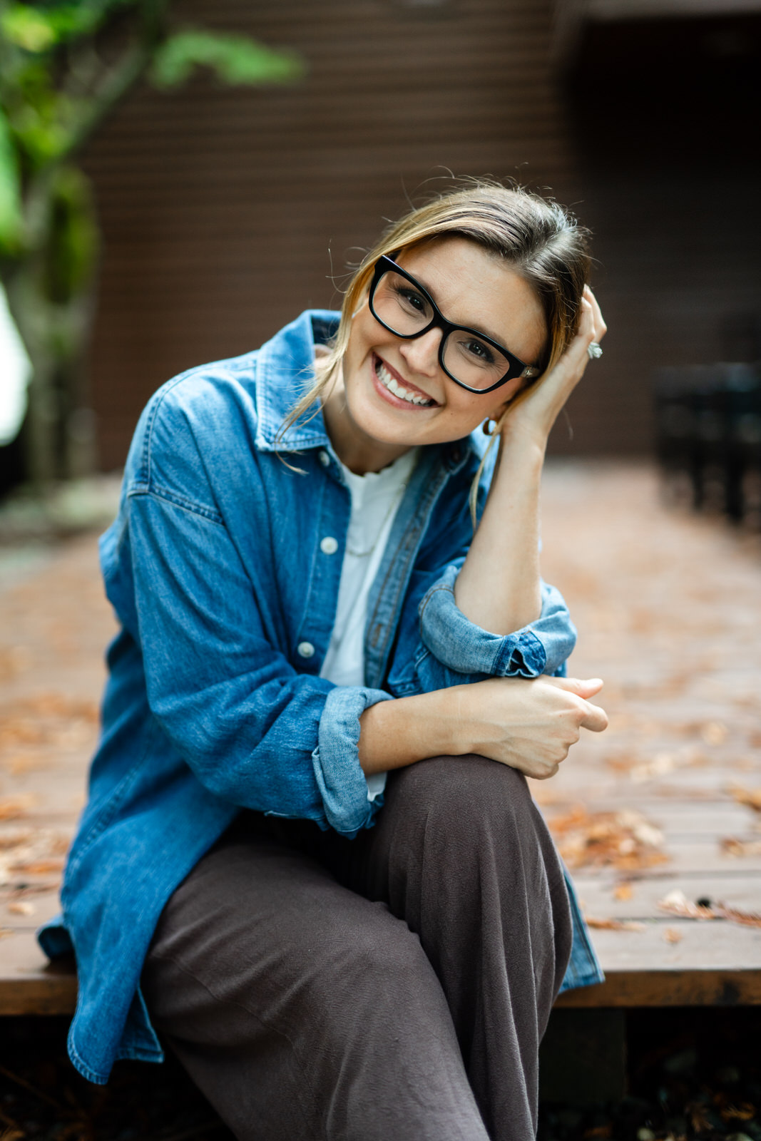 women in jean top with glasses sitting on a deck and hand on her head